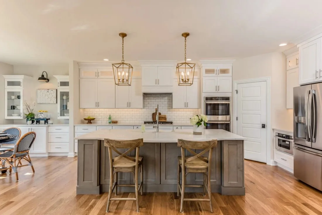 Contemporary kitchen with white cabinets, gold lighting fixtures, and central island.