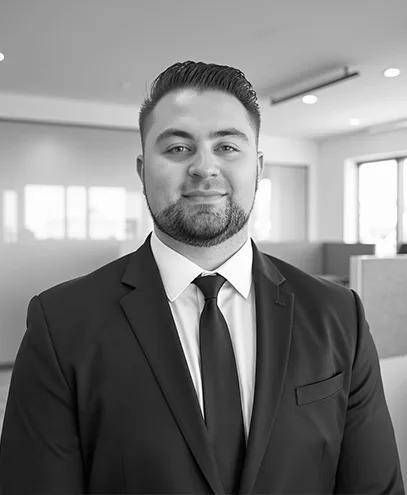 Formal portrait of a man in a black suit and tie, looking into camera.