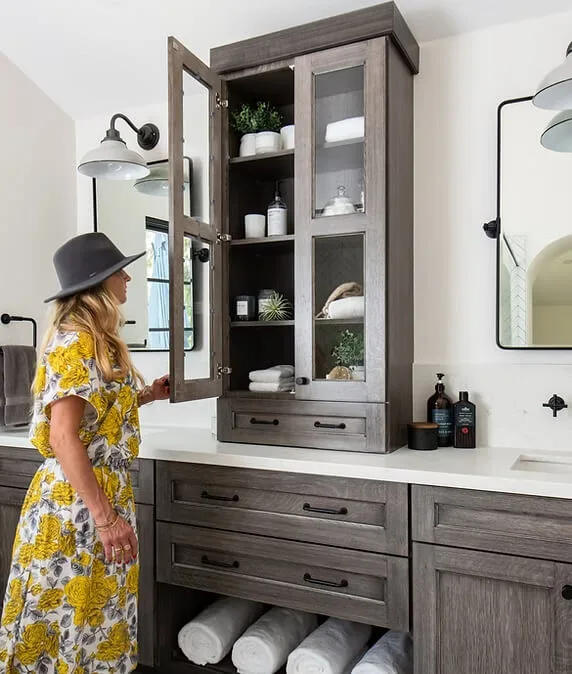 Woman in a floral dress standing in a modern bathroom with dual vanities and open shelving.