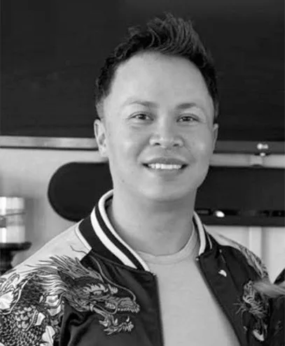Black-and-white close-up portrait of a cheerful man in a patterned jacket.