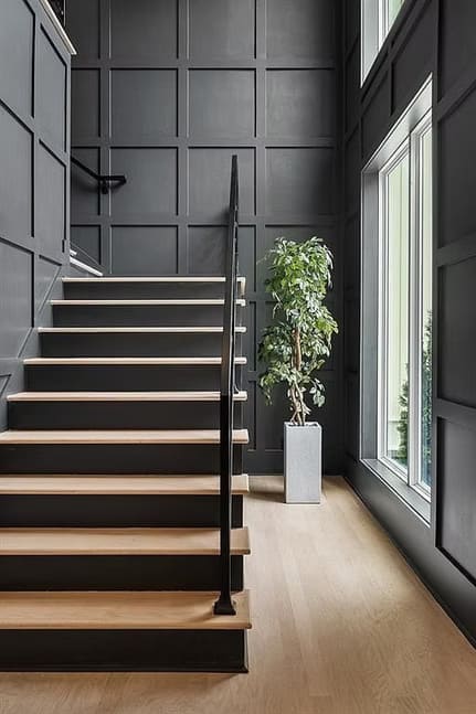 Modern staircase with black railing, wooden treads, and a potted plant.