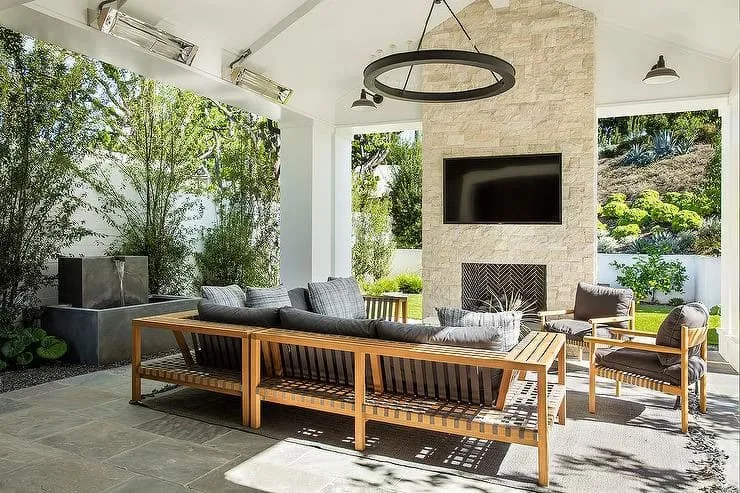 Outdoor patio with wooden furniture, cushions, and ceiling fan under a white structure.