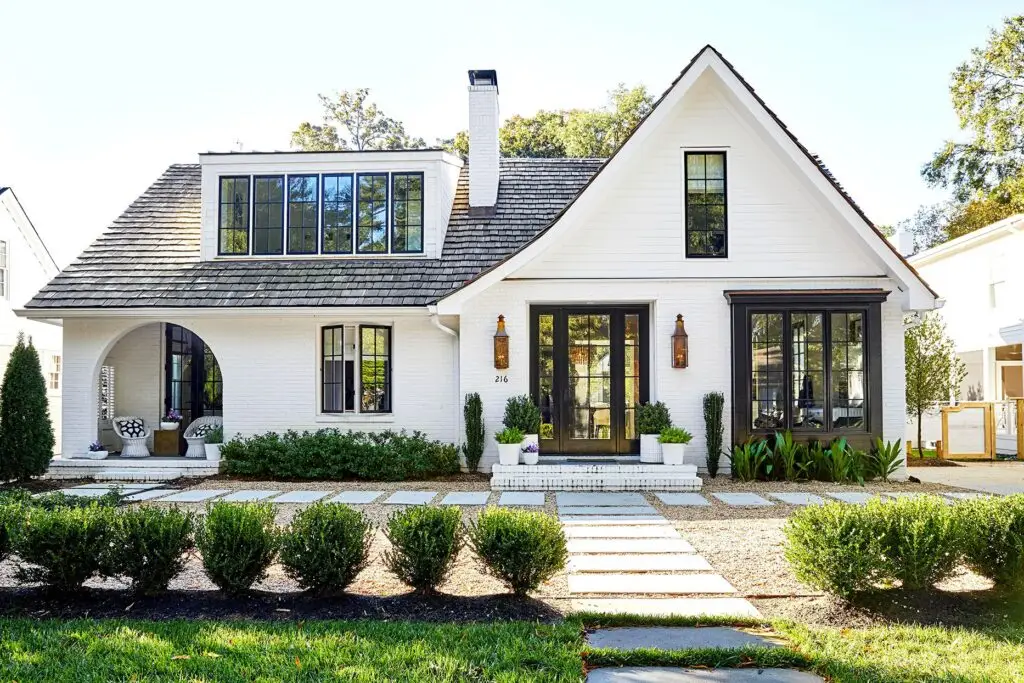 Charming white house with black trim, lush lawn, and stone path.