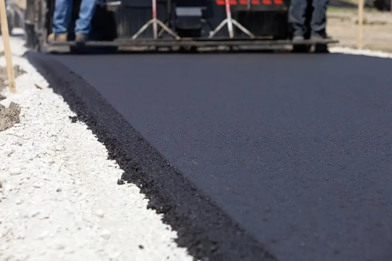 Close-up of a straight edge of freshly laid black asphalt on a light gravel base.