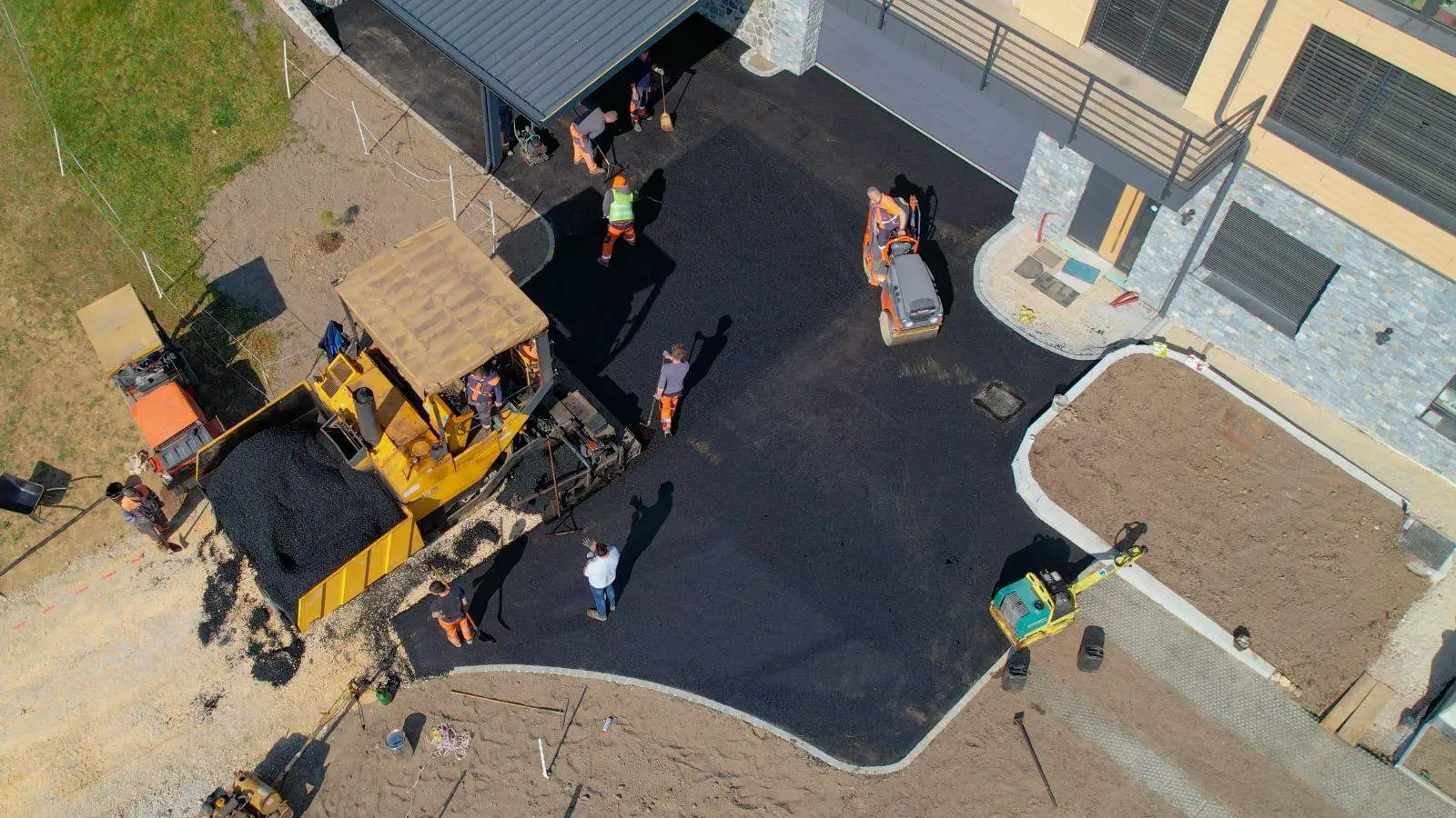 Aerial view of construction workers paving a driveway with asphalt near a building.