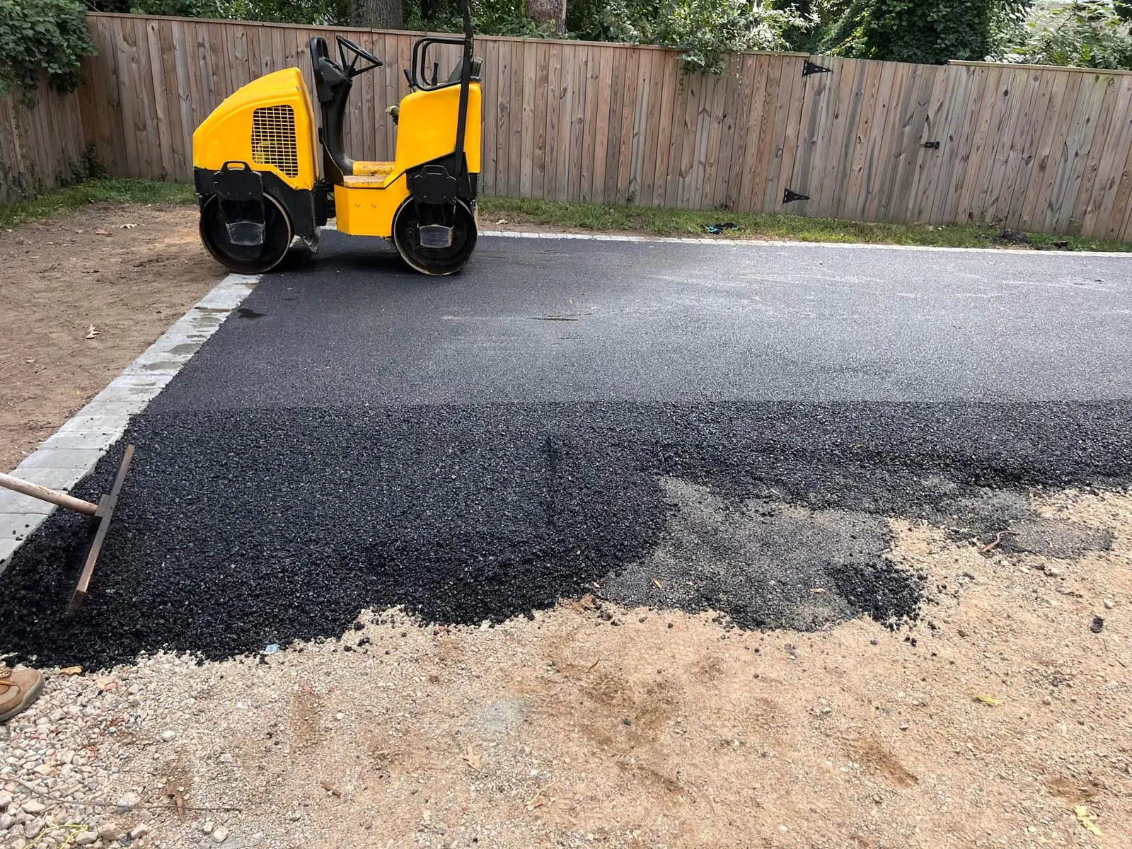 Yellow steamroller compacting newly laid asphalt on a residential driveway.