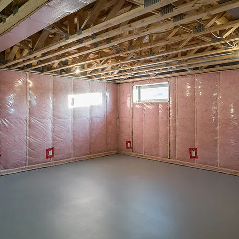 Unfinished Basement: A wide shot of a basement during the construction phase, showing pink insulation on the walls and exposed ceiling joists.