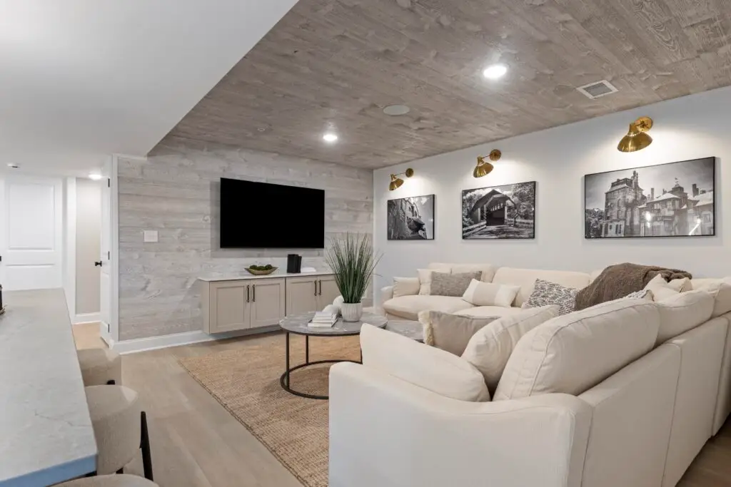 Modern Basement Lounge: A finished basement featuring a wall-mounted TV, white sectional sofa, and recessed lighting.