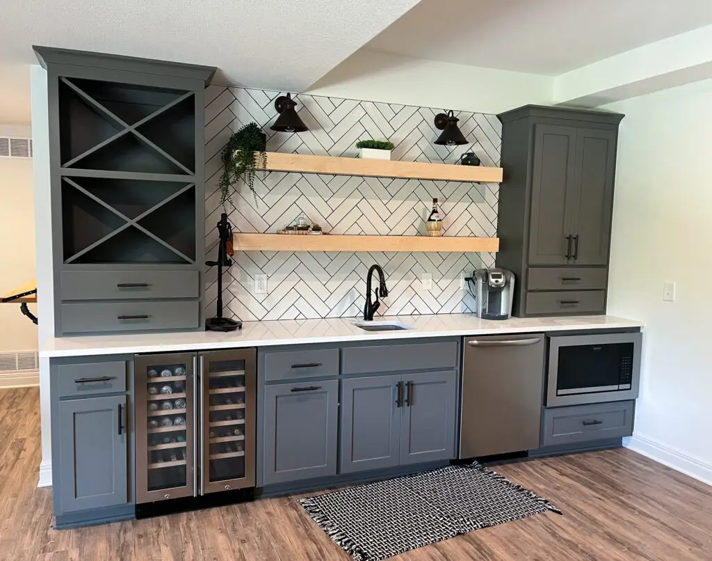 Modern Wet Bar: A sleek home bar area with gray cabinets, a herringbone backsplash, floating wooden shelves, and a built-in wine fridge.