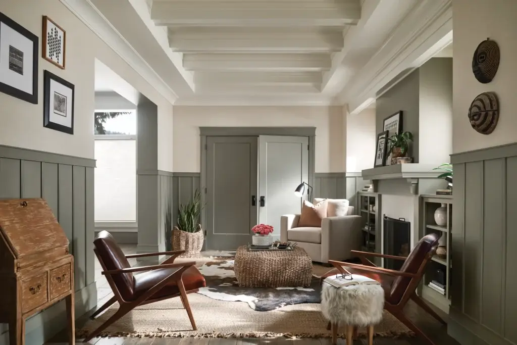 Cozy Craftsman-style living room with exposed beams, green wainscoting, armchairs, and a woven ottoman.