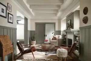 Cozy Craftsman-style living room with exposed beams, green wainscoting, armchairs, and a woven ottoman.