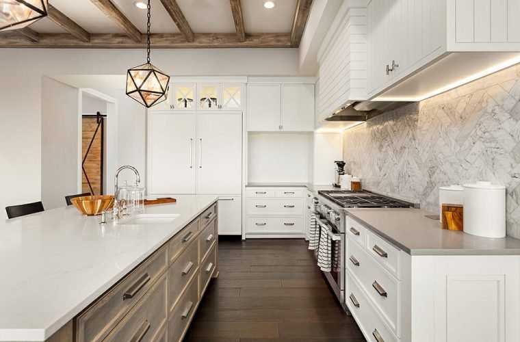 Spacious white kitchen with marble backsplash, pendant lighting, and dark wood flooring.