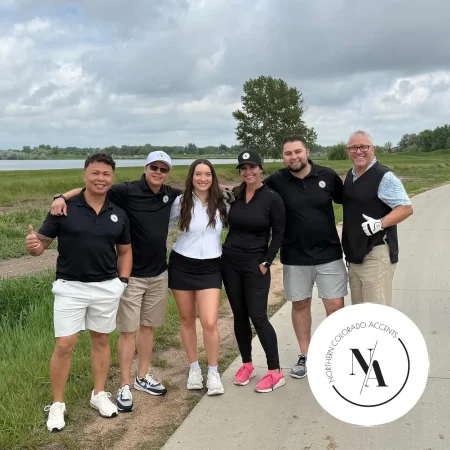 Team of five people posing on a sidewalk in front of a scenic outdoor backdrop with company logo watermark.